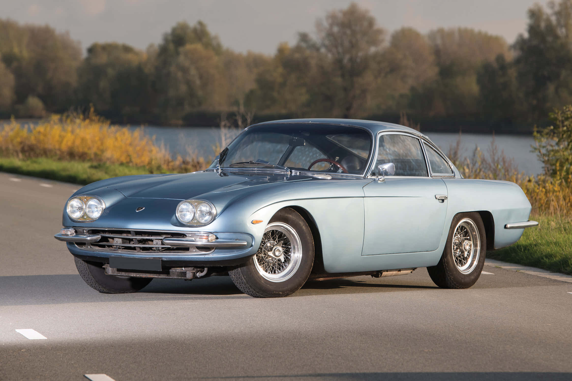 Lamborghini 400 Gt 桌布 壁紙 — 一輛淺藍色復古跑車配備鋼絲輪圈，在秋葉環繞的湖邊道路上行駛。
