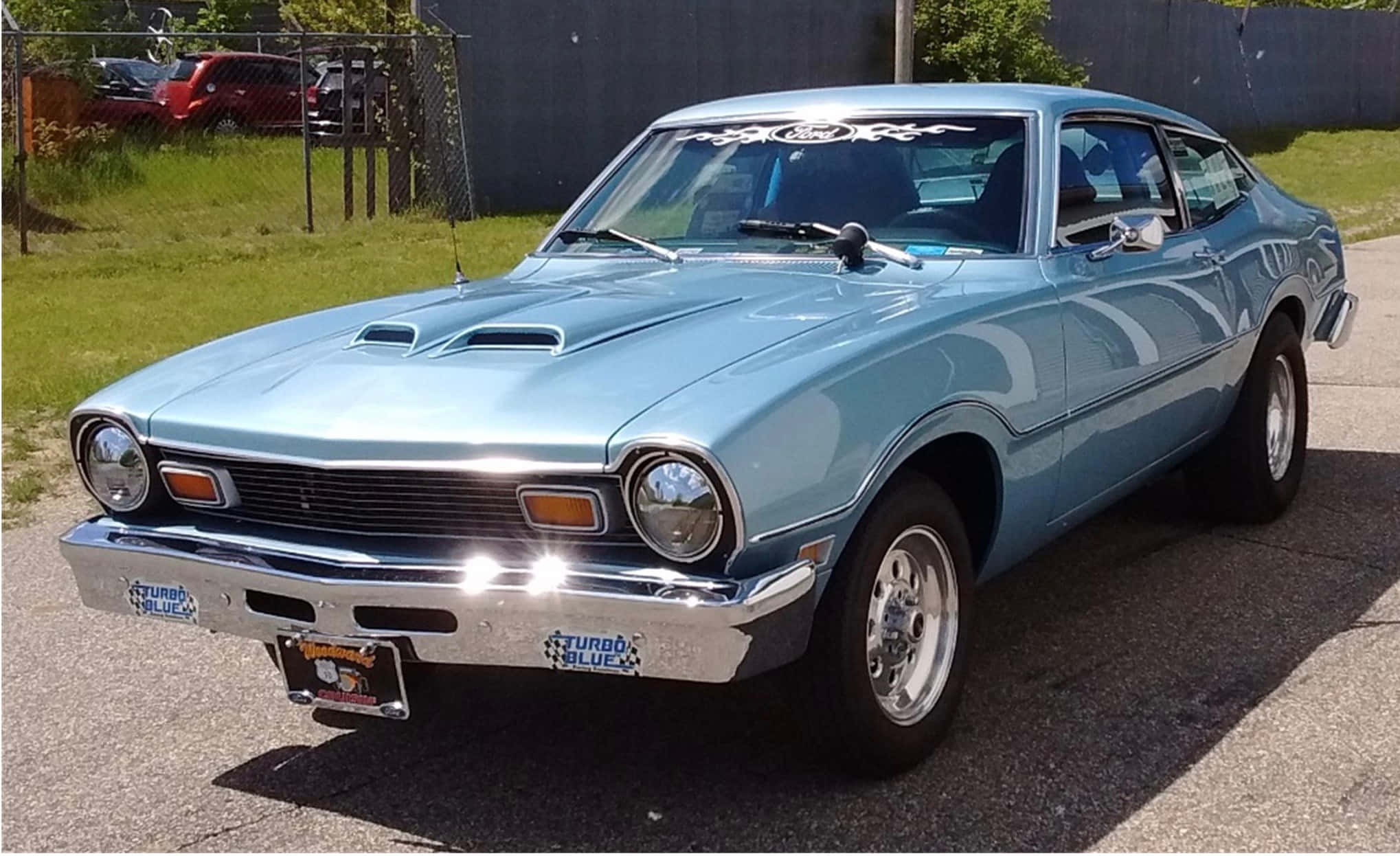 Ford Maverick 桌布 壁紙 — 一輛淺藍色經典肌肉車，帶有鍍鉻飾邊和引擎蓋進氣口，停在陽光普照的瀝青路面上。