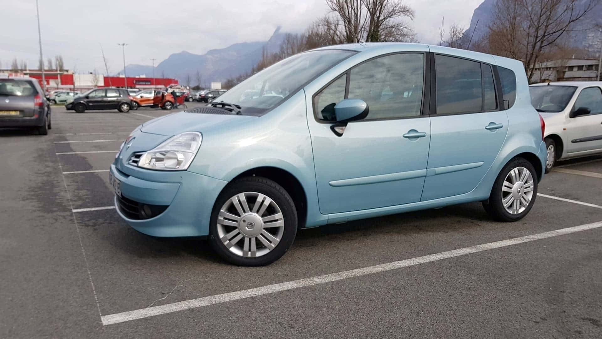 Renault Modus 桌布 壁紙 — 一輛淺藍色雷諾Grand Scenic停放在停車場，背景有山脈，天空多雲。