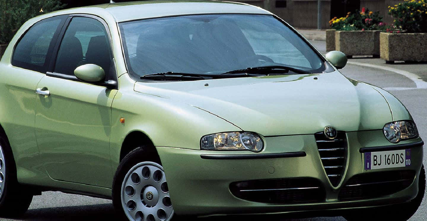 Alfa Romeo 147 桌布 壁紙 — 一輛淺綠色的Alfa Romeo 147掀背車停在鋪砌的街道上，背景有花盆。