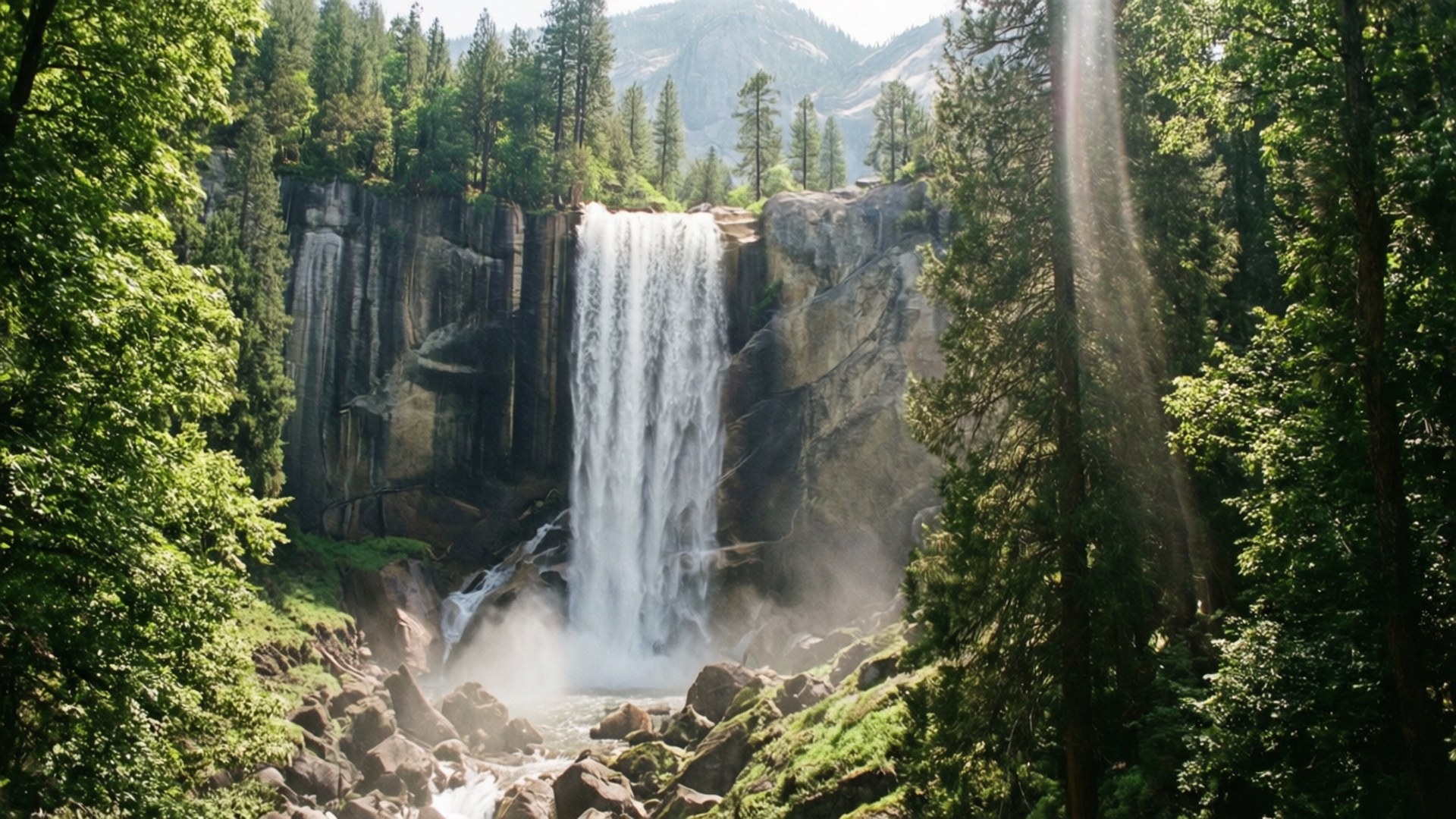 Spring Yosemite Falls 壁紙 — 一道強勁的瀑布從岩石懸崖上傾瀉而下，周圍是茂密的綠色森林，陽光穿過樹林照射進來。