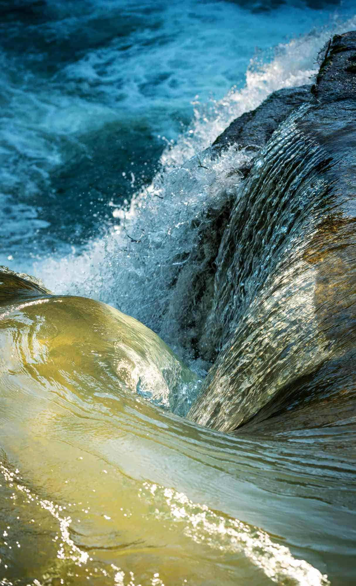 Best iPhone 桌布 壁紙 — 強勁的海浪拍打著黑色的岩石，在明亮的陽光下將白色的浪花噴向空中。
