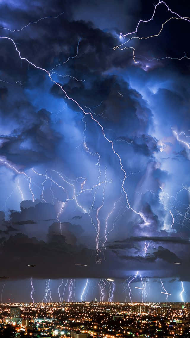 Lightning iPhone 桌布 壁紙 — 強烈的閃電在暴風雨的夜空中劈啪作響，照亮了由無數燈光點綴的廣闊城市景觀。