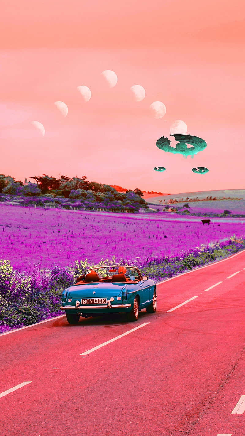  壁紙 — 一輛青綠色敞篷車在粉紅色天空下，沿著一條紅色道路穿過超現實的紫色田野，天空中有漂浮的月亮和UFO。