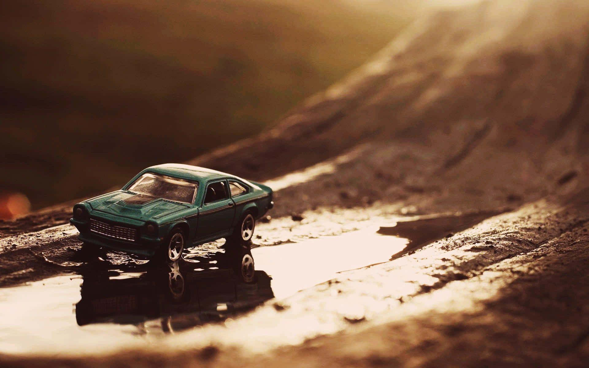  壁紙 — 一架青綠色玩具車放在泥路淺水坑中，沐浴在溫暖的金色夕陽下。