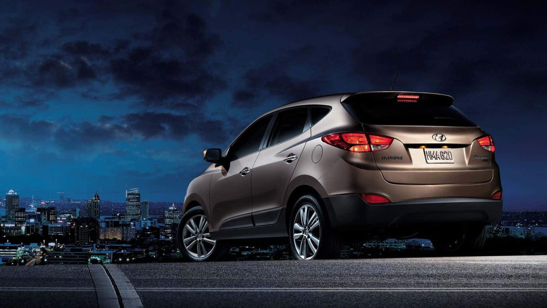 Hyundai Tucson 桌布 壁紙 — 一輛青銅色現代Tucson SUV在夜間停泊在天台上，俯瞰著黑暗多雲天空下閃爍的城市天際線。