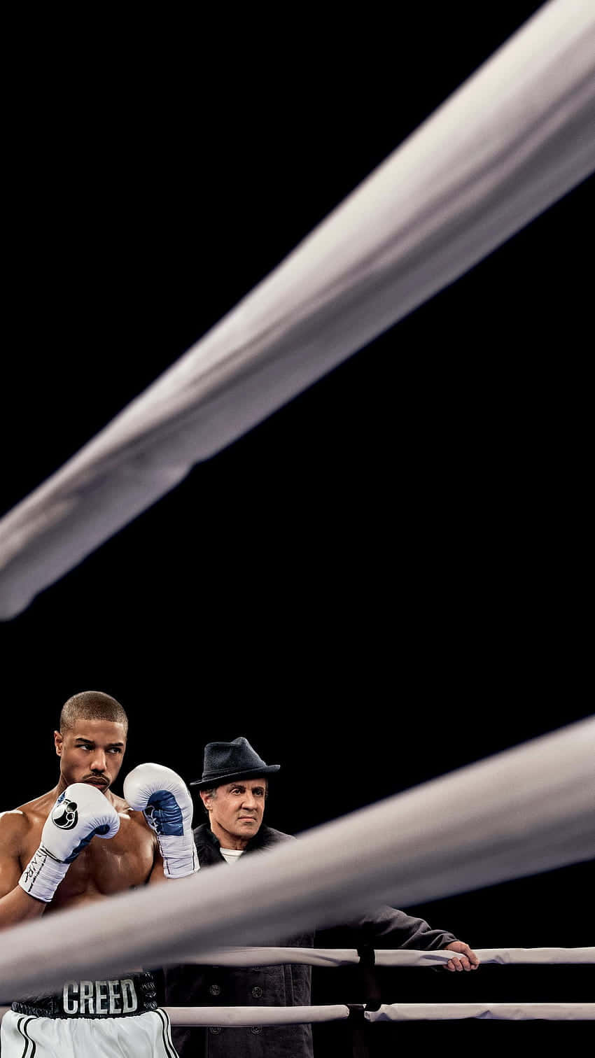  壁紙 — 一名戴著白色手套、穿著 'CREED' 短褲的拳擊手在擂台上警覺地站著，他的導師在繩索旁專注地觀看，背景是純黑色。