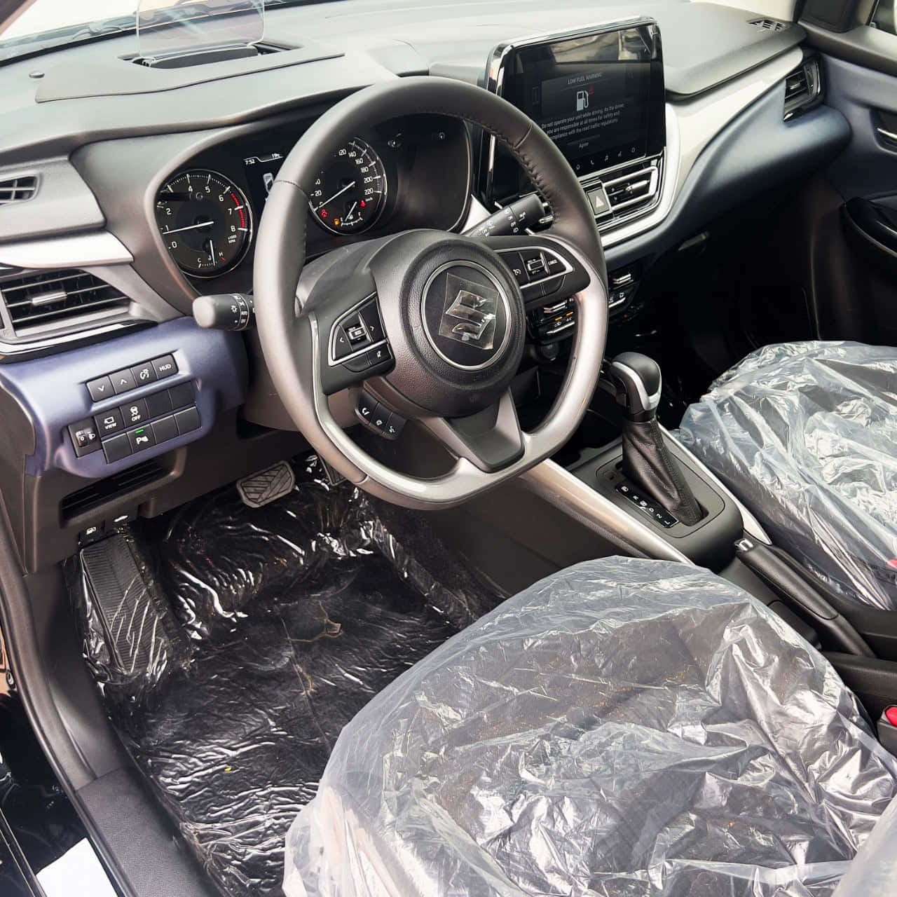 Suzuki Baleno 桌布 壁紙 — 全新鈴木汽車內部，座椅和地板有塑膠保護套，顯示方向盤、儀表板和排檔桿。
