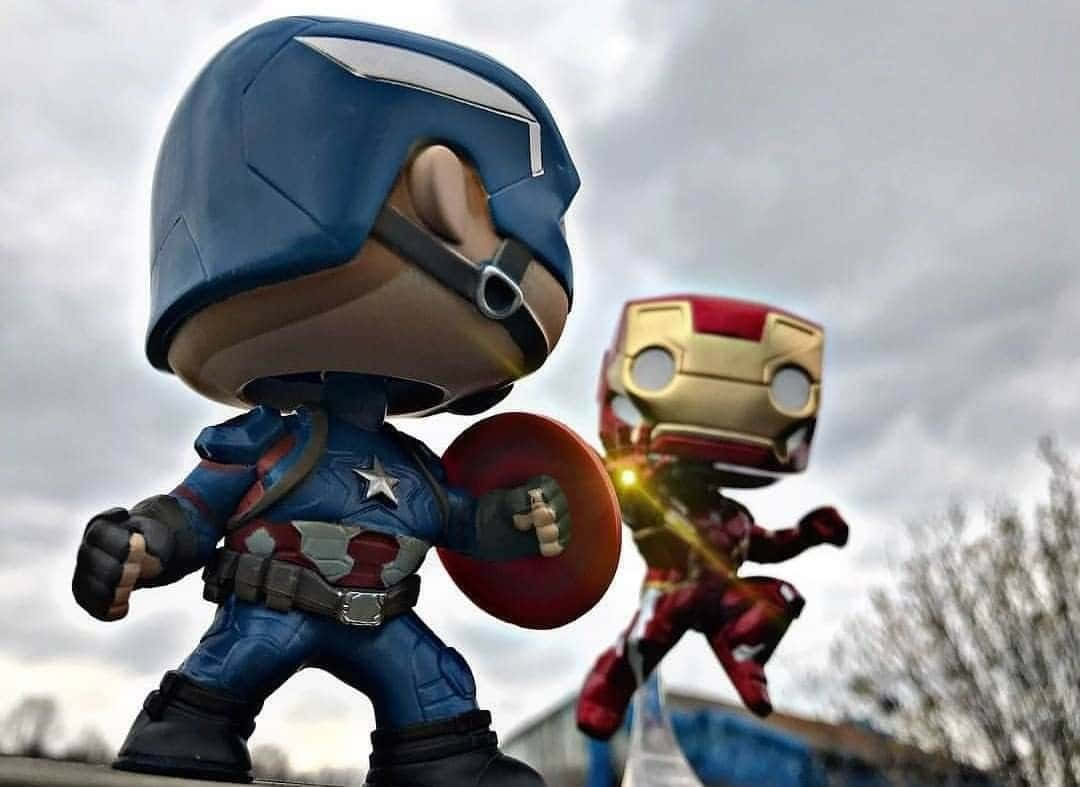 Iron Man Pop Figures 桌布 壁紙 — Q版美國隊長和鋼鐵人公仔在陰天背景下，以英雄姿態擺出姿勢，背景有光禿的樹木。