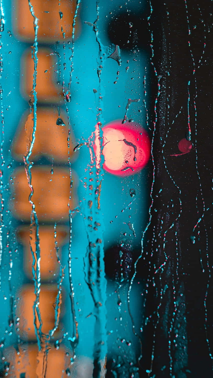  壁紙 — 雨水沿窗流下，顯露出模糊的城市景觀，在青綠色和橙色調中有一個發光的粉紅色圓形燈光。