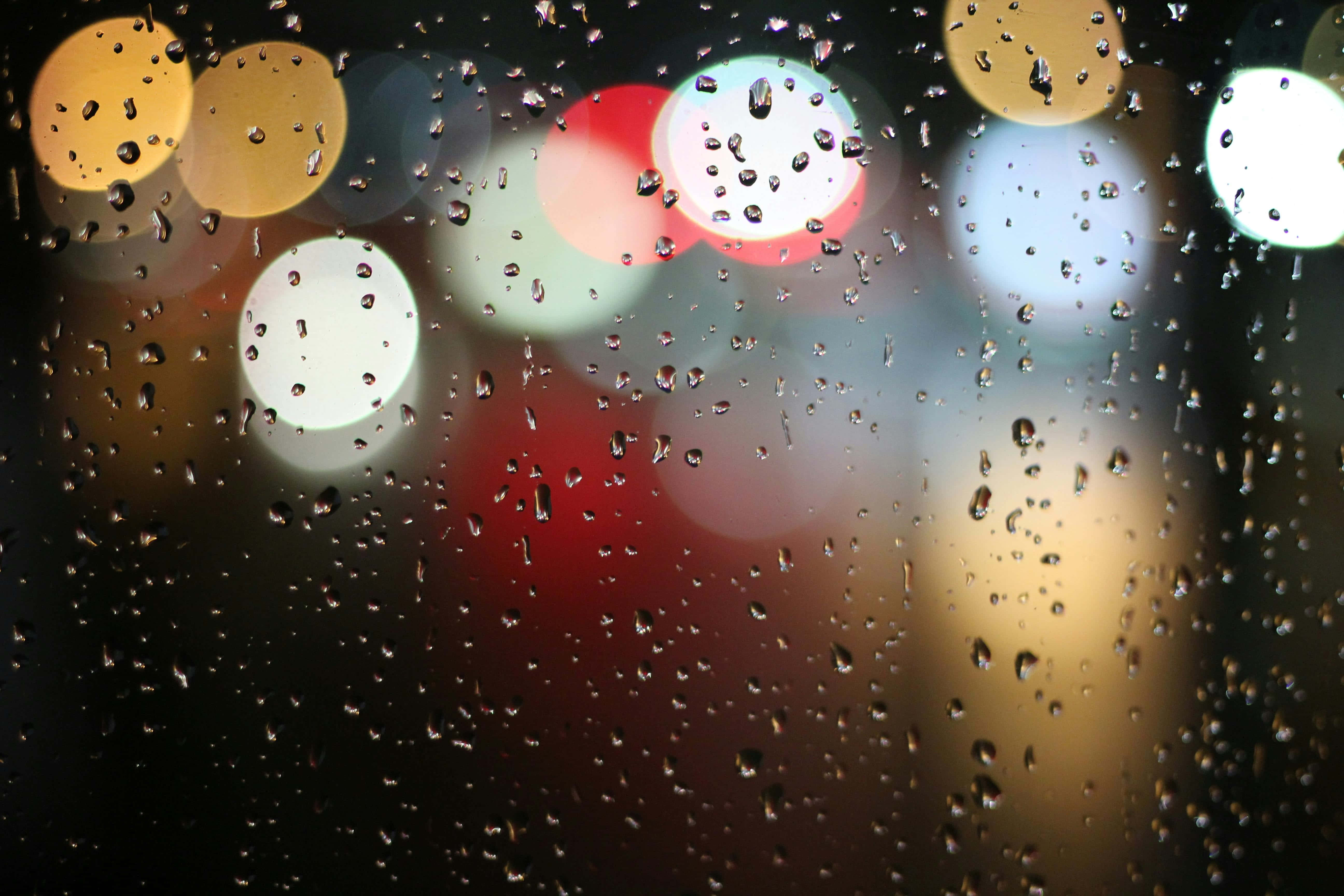 Latest 桌布 壁紙 — 雨滴依附在窗戶上，顯露出模糊的城市燈光，以溫暖的紅色、黃色和白色閃爍。