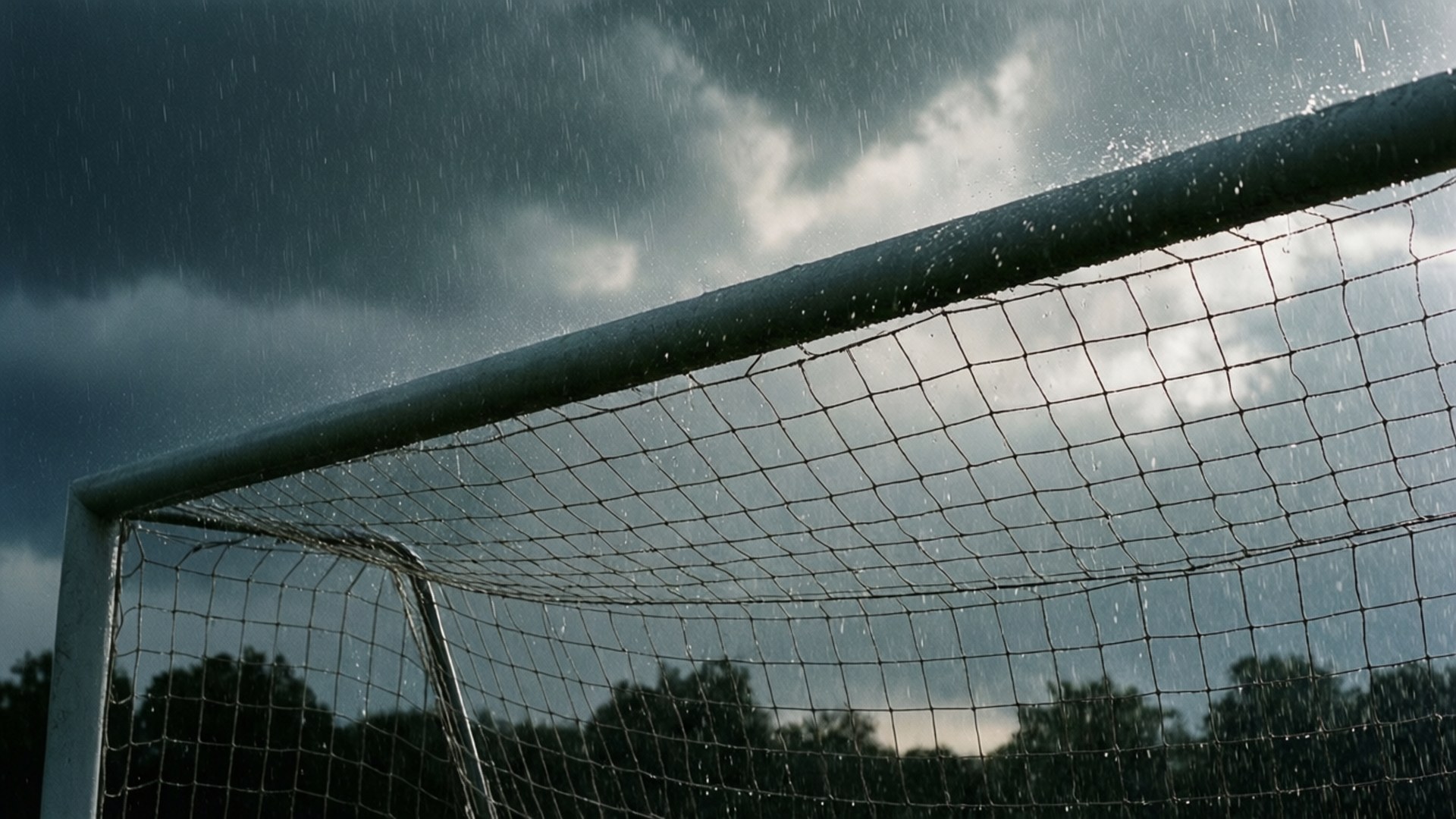 Goal Post 桌布 壁紙 — 雨滴沿著足球球門網流下，下方是黑暗風暴天空和剪影樹木。