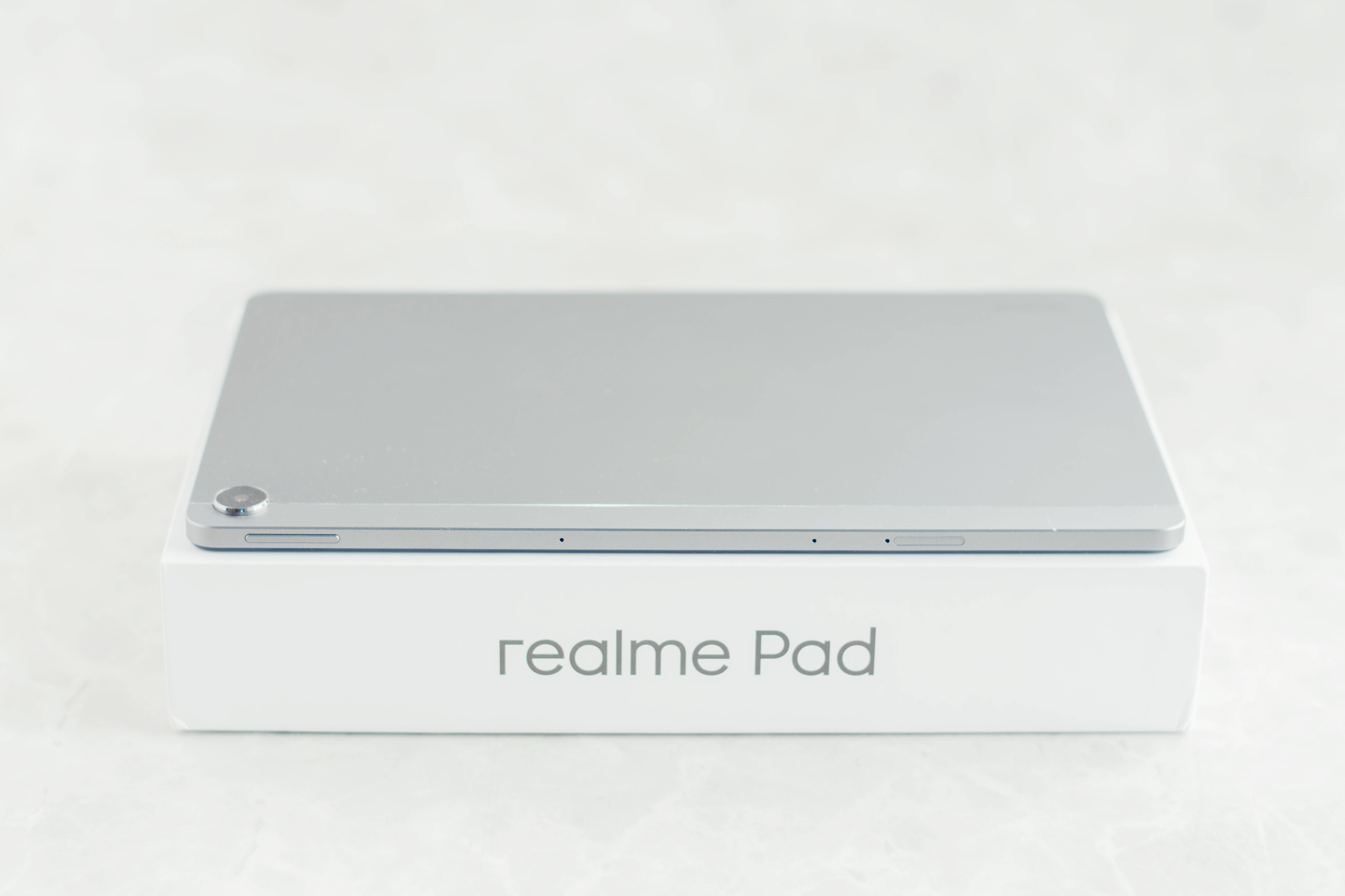 Realme Pad 灰色 壁紙 — 一部時尚的銀色 realme Pad 平板電腦放在其白色品牌盒子上，背景為柔軟的紋理。