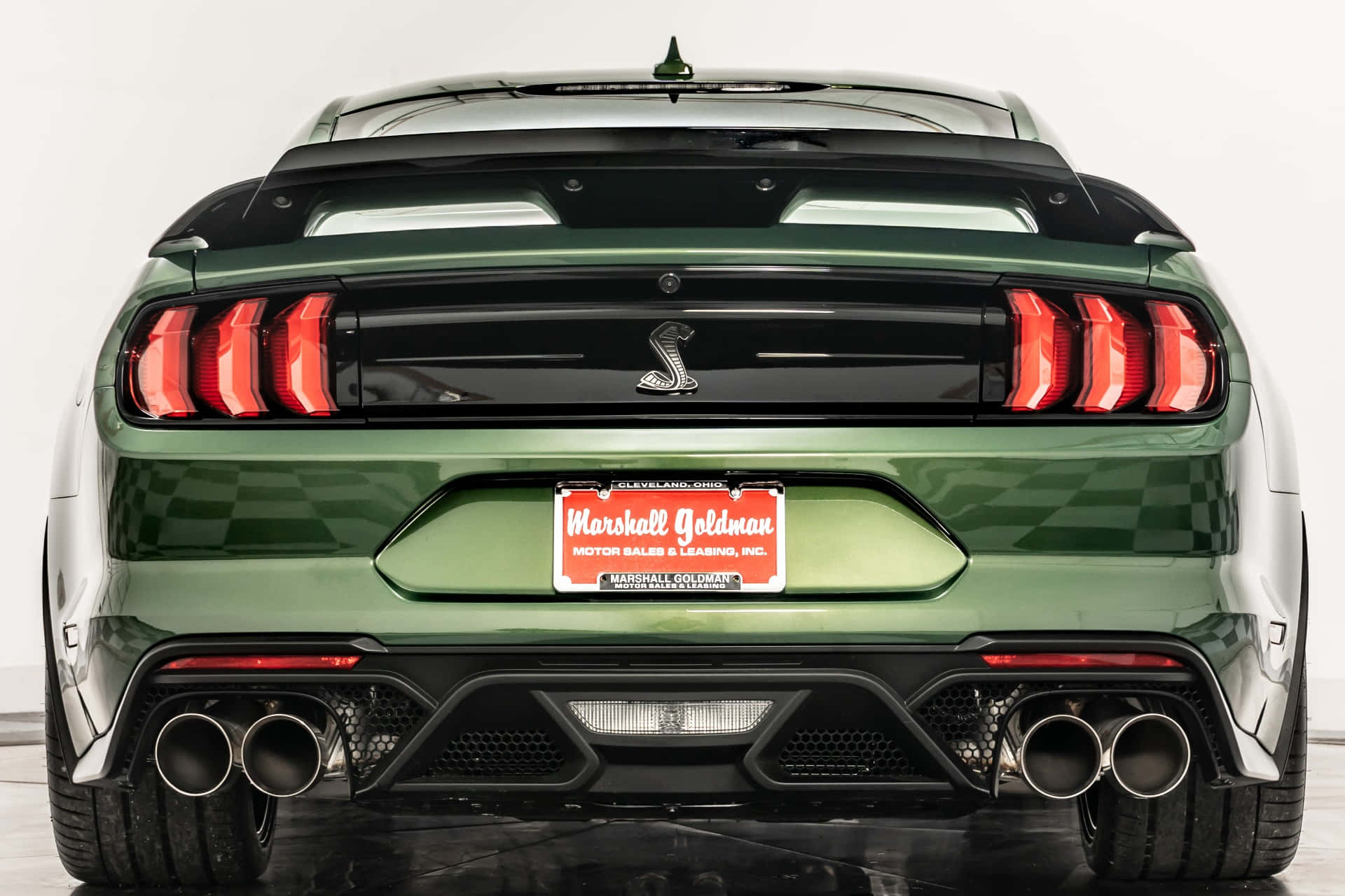  壁紙 — 綠色福特 Mustang Shelby GT500 的後視圖，帶有紅色尾燈和四出排氣管，背景為白色工作室。