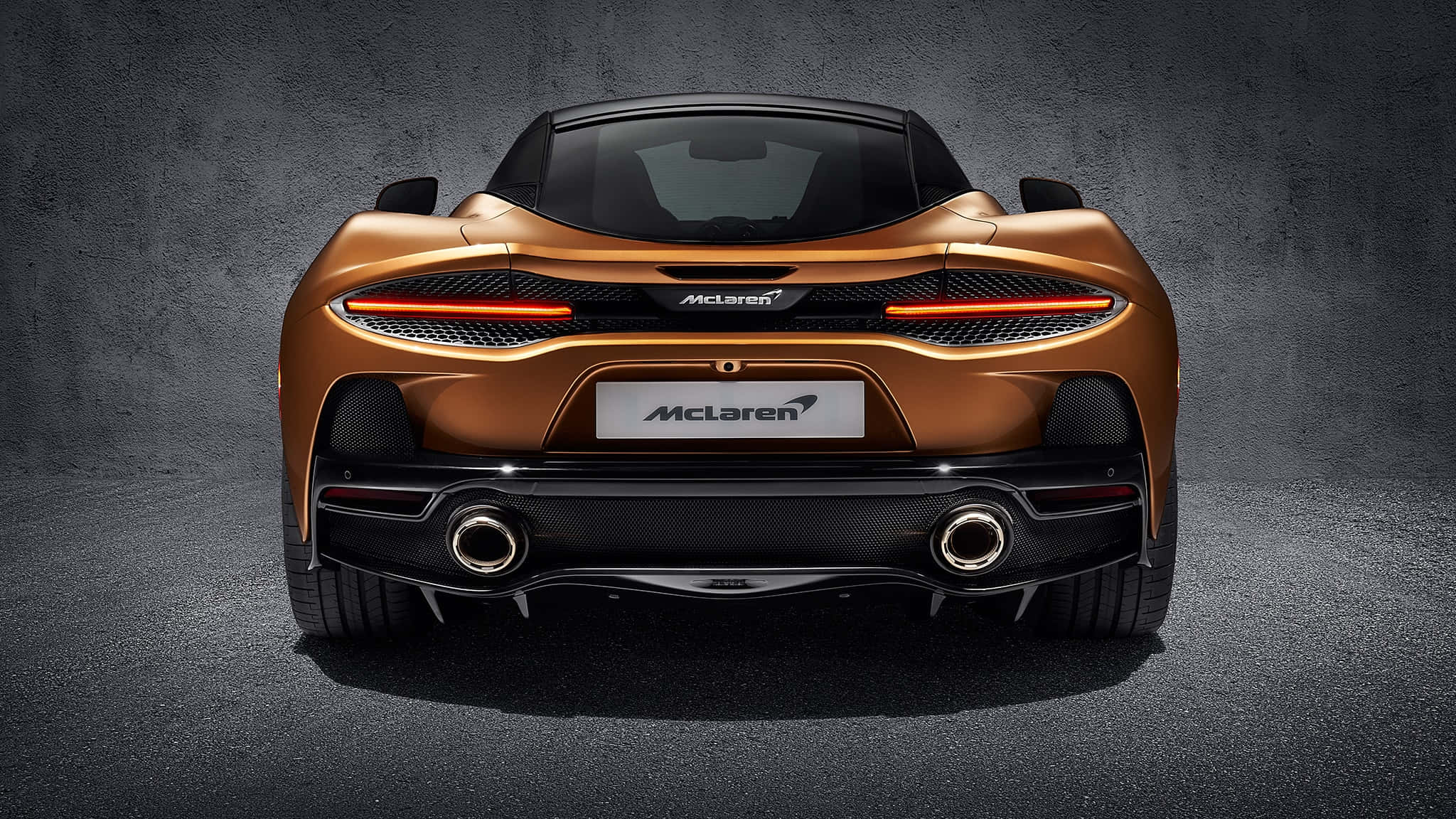 Mclaren Gt 桌布 壁紙 — 一輛銅色麥拿倫跑車的後視圖，尾燈發光，背景是深色紋理的工作室牆壁。