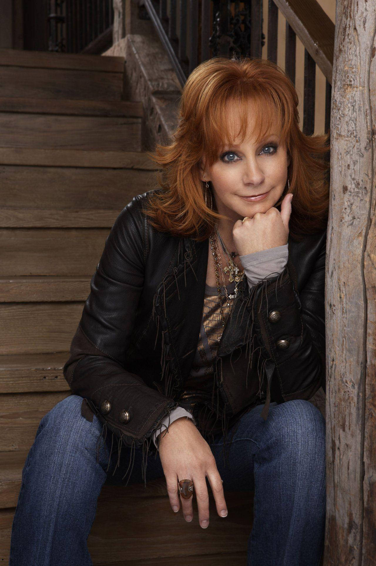 Celebrity 桌布 壁紙 — Reba McEntire 隨意地坐在木樓梯上，穿著帶流蘇的皮夾克和牛仔褲，露出溫暖的笑容。