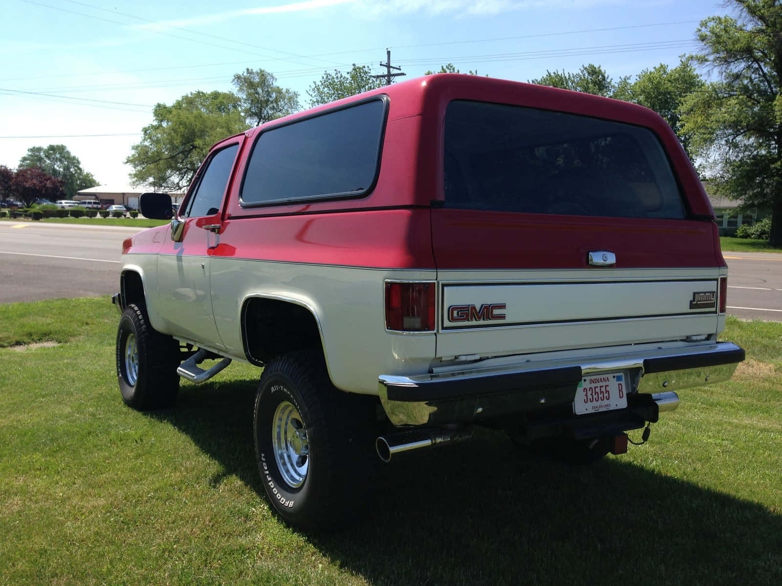 Gmc Jimmy 桌布 壁紙 — 一輛紅色和白色的升高GMC Jimmy SUV停放在草地上，背景是晴朗的天空和樹木。