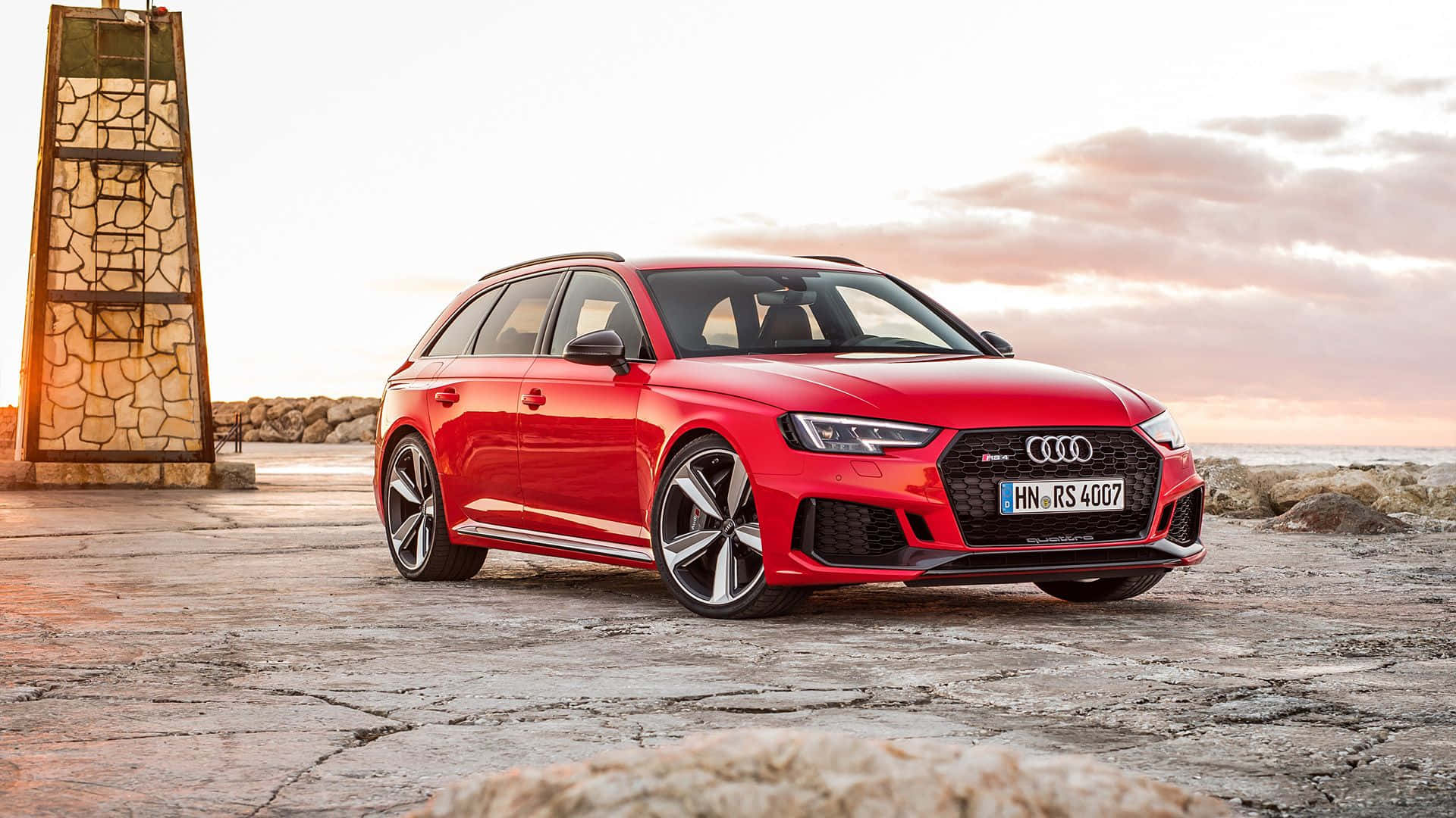 Audi Rs4 桌布 壁紙 — 一輛鮮紅色的奧迪RS4 Avant旅行車停泊在日落時分龜裂的混凝土碼頭上，旁邊有一座石塔。