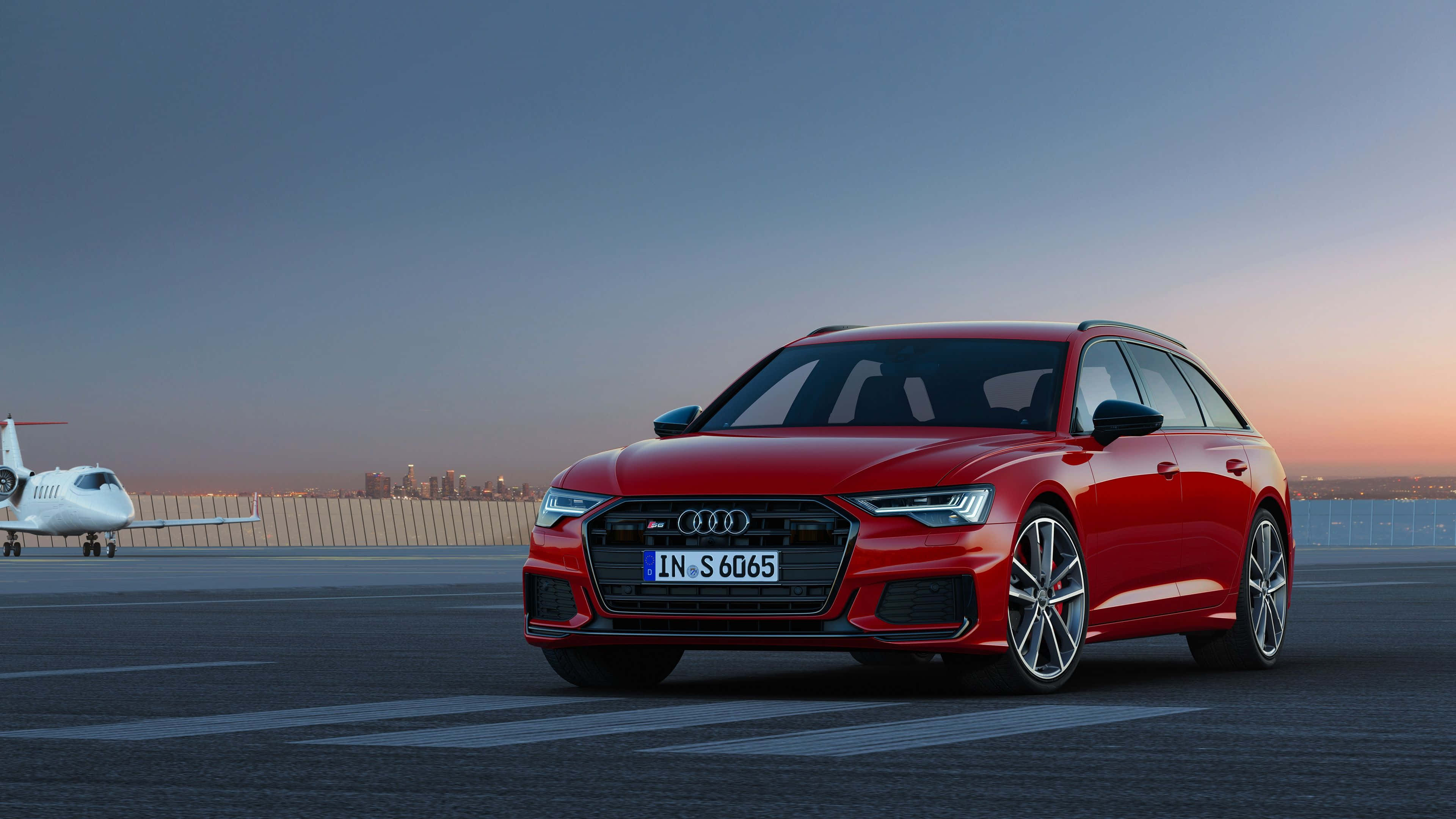 Audi A6 桌布 壁紙 — 一輛時尚的紅色奧迪旅行車停在機場停機坪上，背景是日落時分的私人飛機。