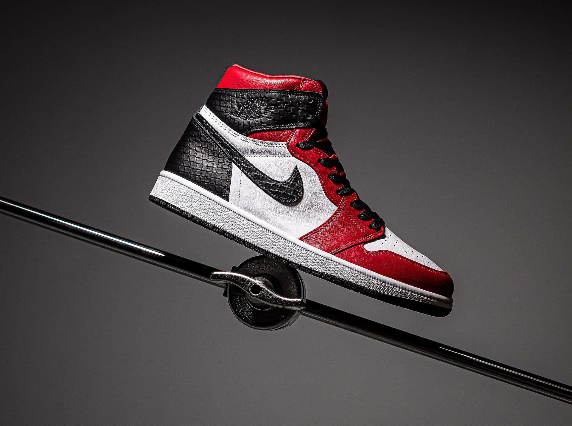 紅、黑、白三色高筒運動鞋在攝影棚燈光下平衡在黑色桿子上。 — Air Jordan 壁紙