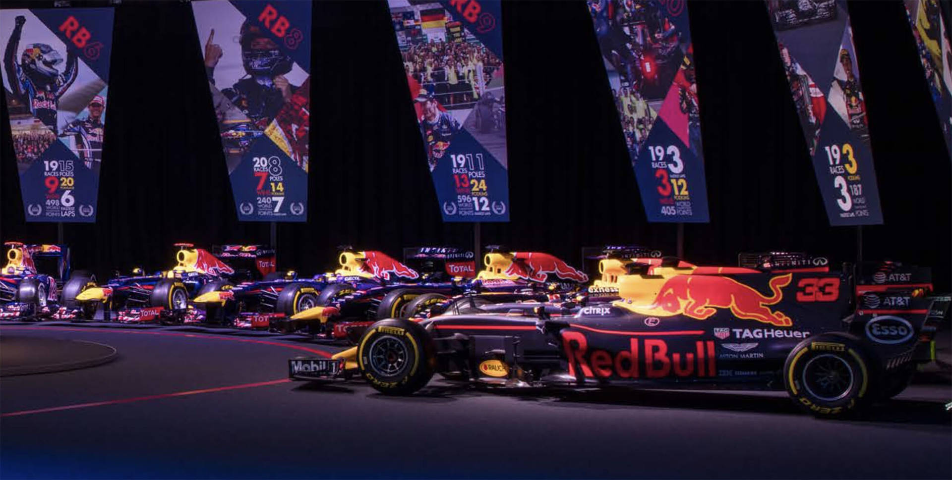 Red Bull F1 賽車在舞台上展示，背景有冠軍旗幟。 — 紅牛F1 壁紙