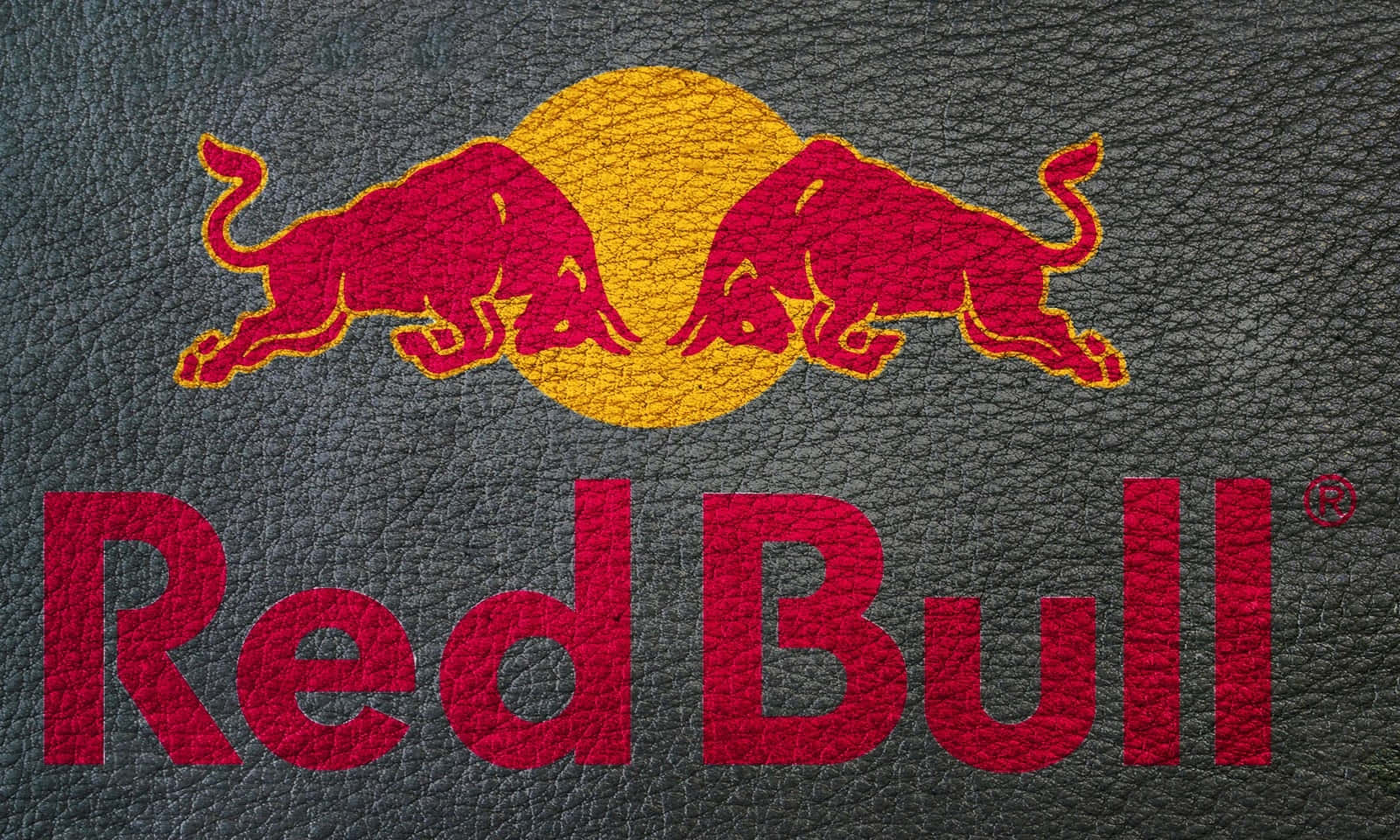 紅牛 桌布 壁紙 — Red Bull 標誌，兩頭紅色公牛在黃色太陽上方相對而立，位於有紋理的深灰色皮革上。