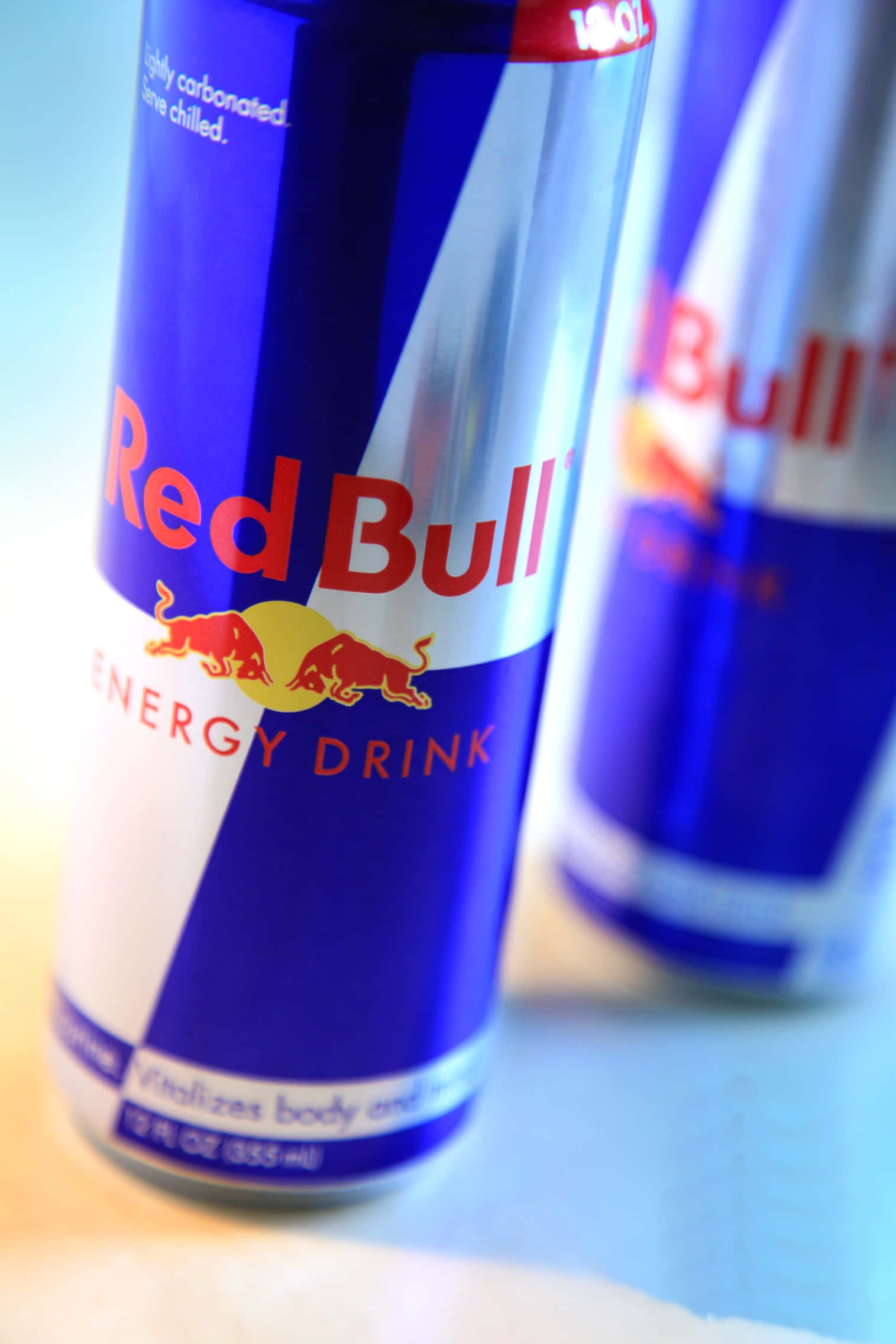 紅牛 桌布 壁紙 — Red Bull 能量飲料罐的特寫，帶有鮮明的紅色和藍色品牌標誌，背景中第二罐模糊不清。