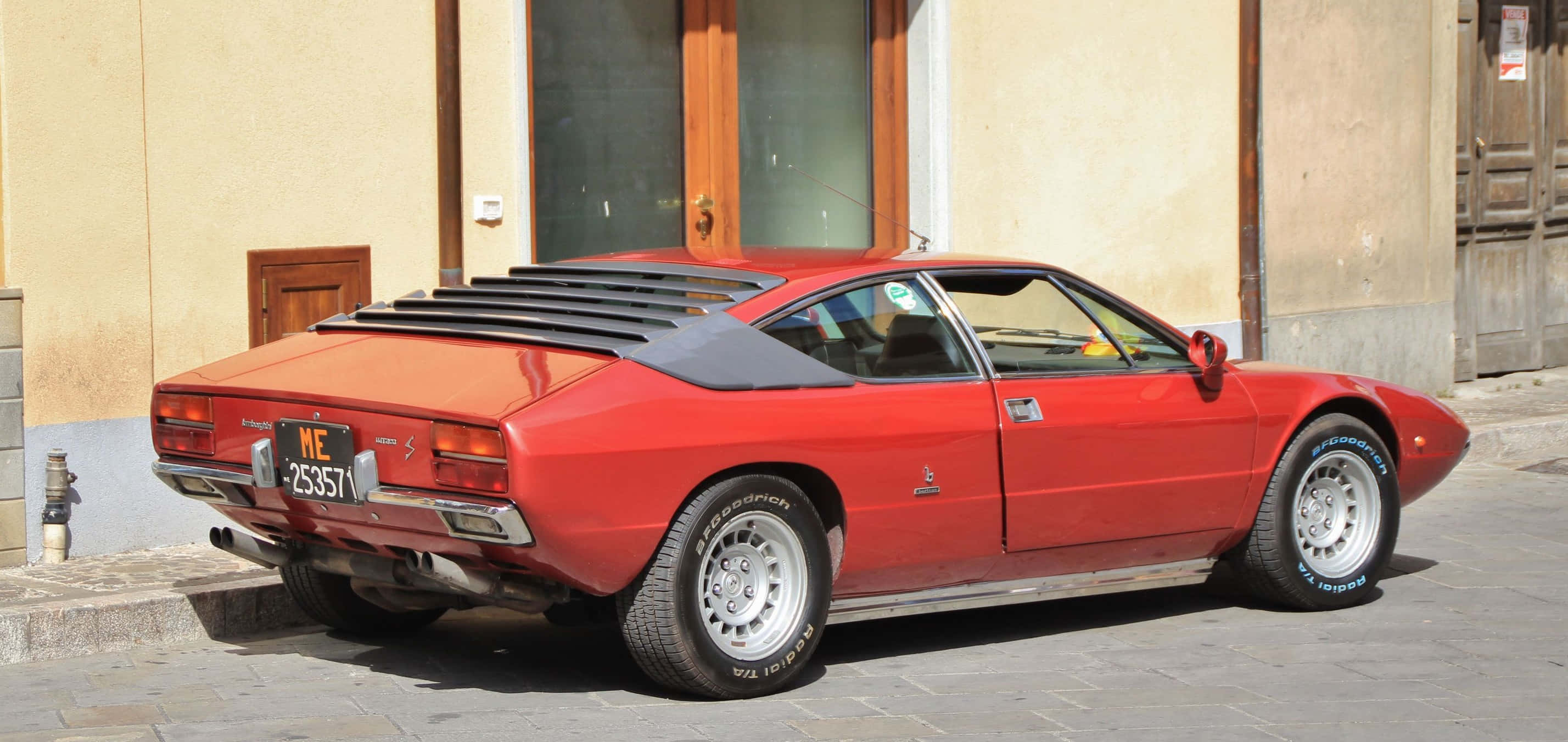Lamborghini Urraco 桌布 壁紙 — 一輛鮮紅色經典法拉利308 GTB停放在陽光普照的鵝卵石街道上，旁邊是一棟米色建築。