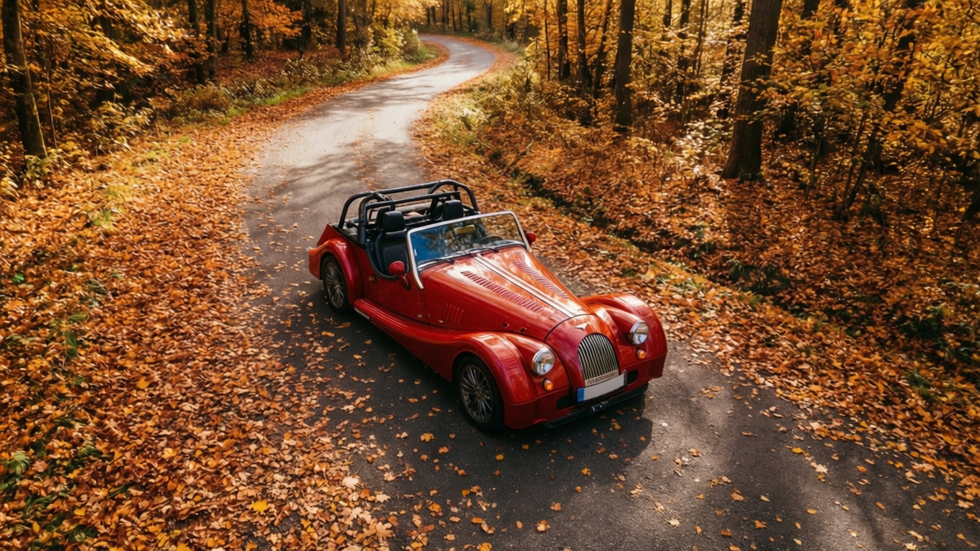 Morgan Roadster 桌布 壁紙 — 一輛鮮紅色的敞篷跑車沿著一條蜿蜒的森林道路行駛，道路鋪滿了金色的秋葉。