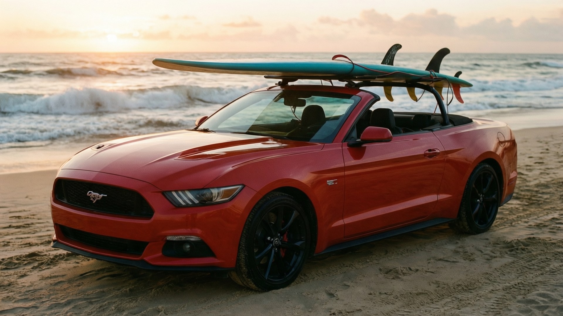 Surf Mustang Sunrise 壁紙 — 一輛鮮紅色敞篷福特野馬，車頂綁著衝浪板，停在日落時分的沙灘上，背後海浪拍打。