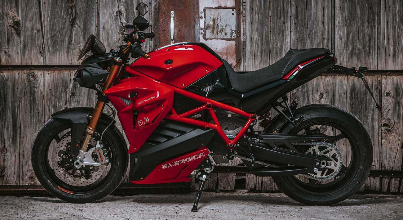  壁紙 — 一台搶眼的紅色Energica EVA電動機車，停放在風化的木製穀倉門前。