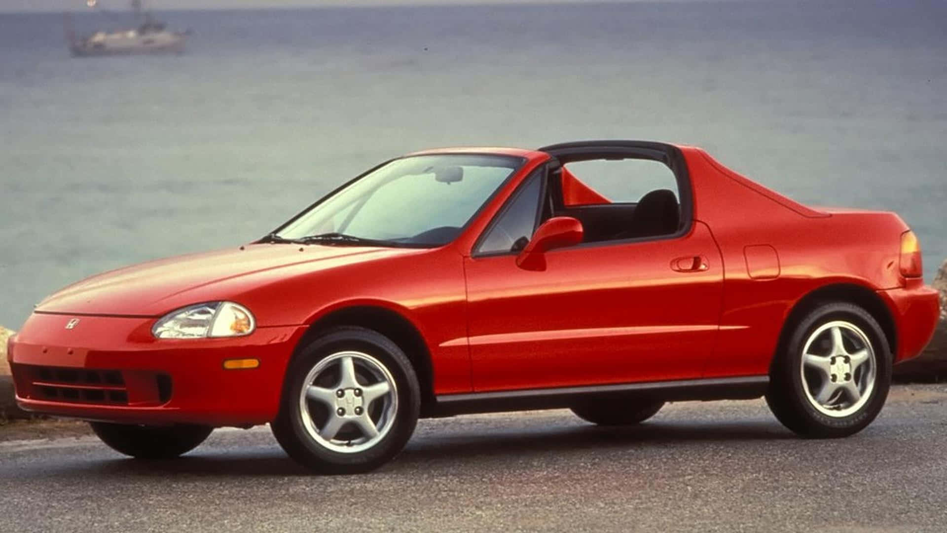 Honda Civic Del Sol 桌布 壁紙 — 一輛鮮紅色的Honda Beat敞篷車停泊在海邊，遠處有帆船。