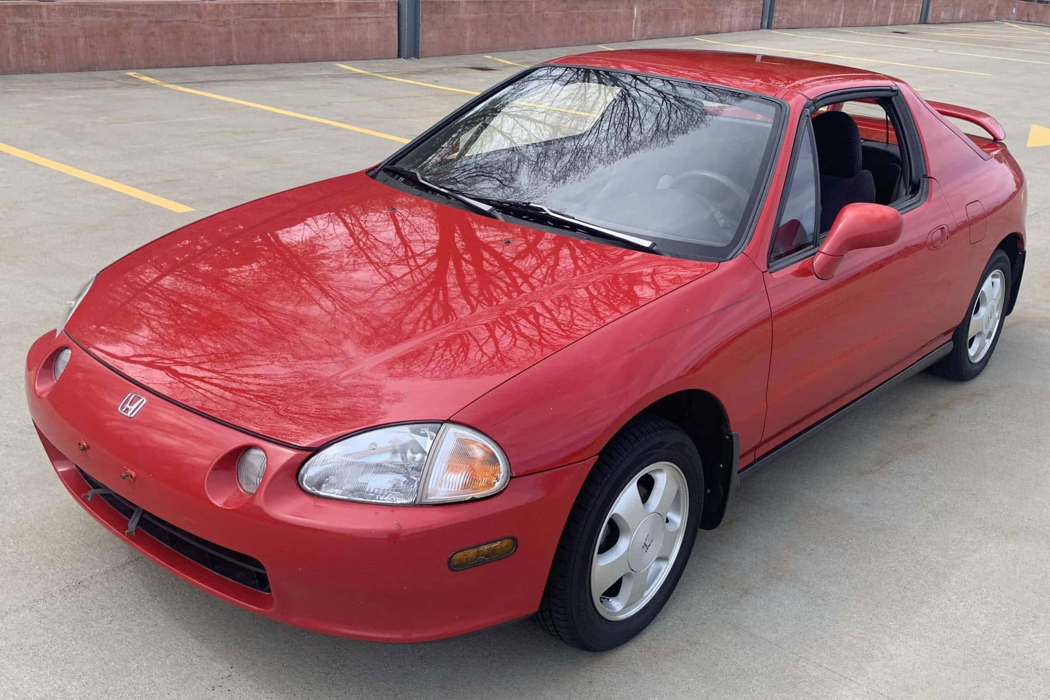 Honda Civic Del Sol 桌布 壁紙 — 一輛鮮紅色的本田 Del Sol 敞篷車停放在混凝土停車場，光禿的樹枝倒映在閃亮的引擎蓋上。