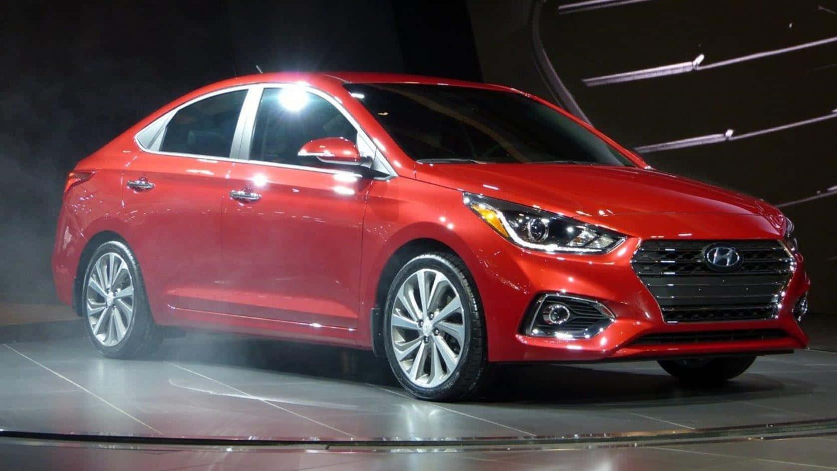 Hyundai Accent 桌布 壁紙 — 一輛閃亮的紅色現代房車在車展演示中，於煙霧繚繞的舞台上，在明亮的聚光燈下閃耀。