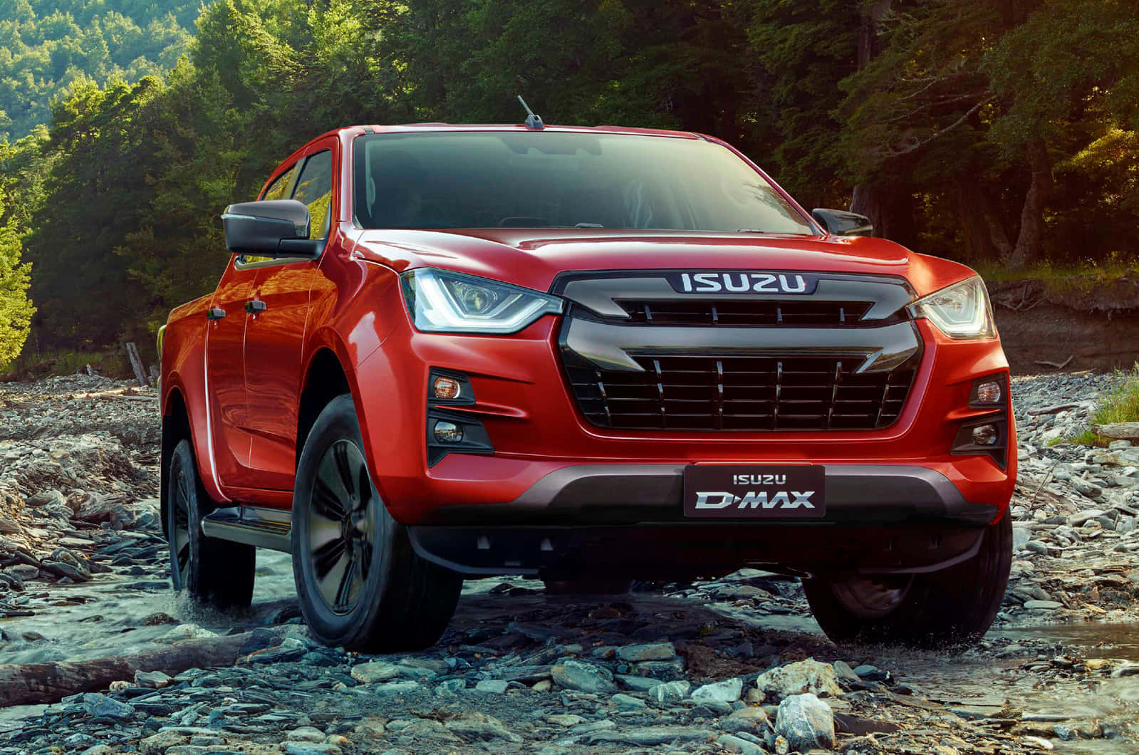  壁紙 — 一輛鮮紅色的Isuzu D-Max皮卡車在金色陽光下行駛在岩石森林溪流中。
