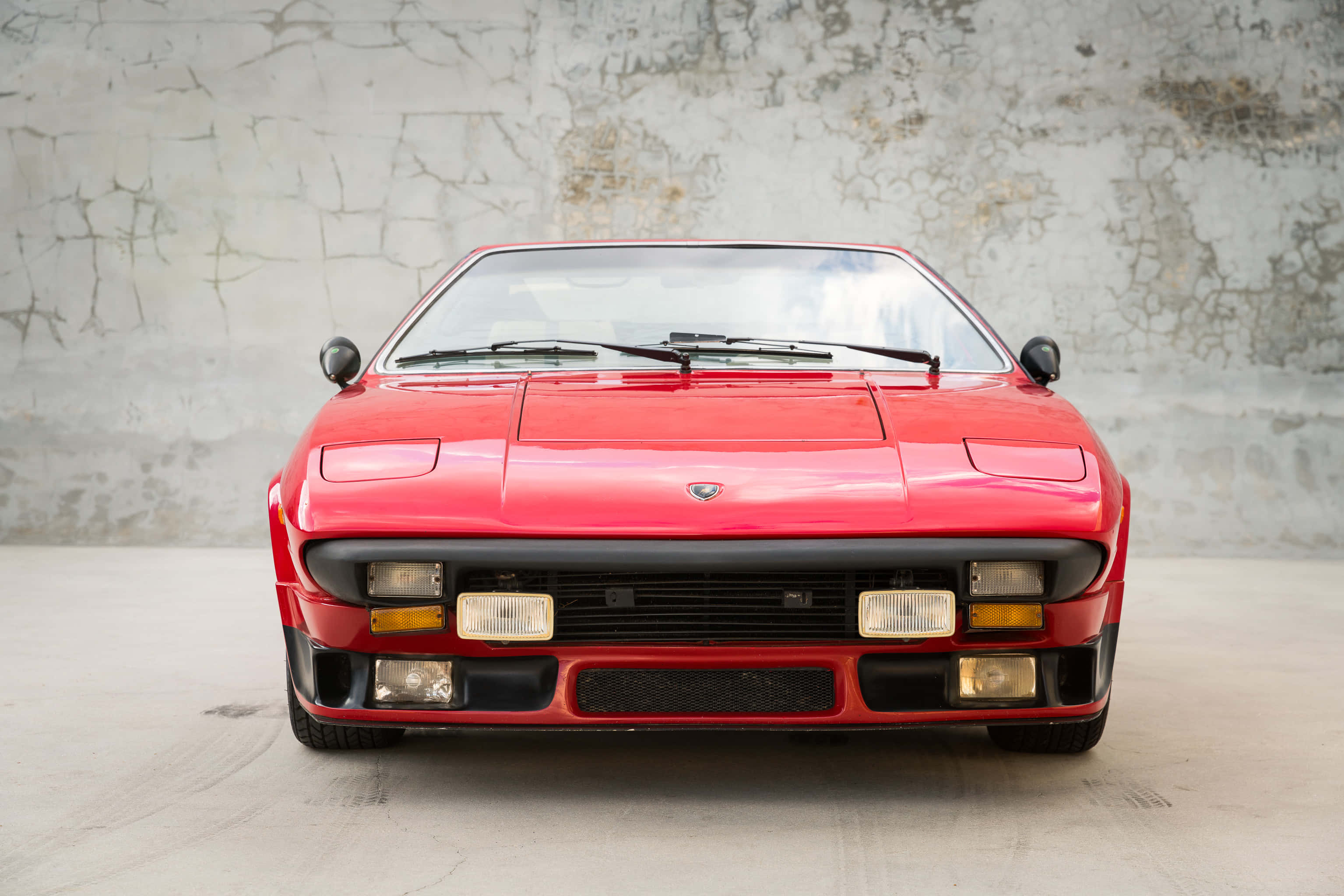 Lamborghini Silhouette 桌布 壁紙 — 一輛鮮紅色的藍寶堅尼Countach在簡約的工作室環境中，正面朝向風化的混凝土牆。