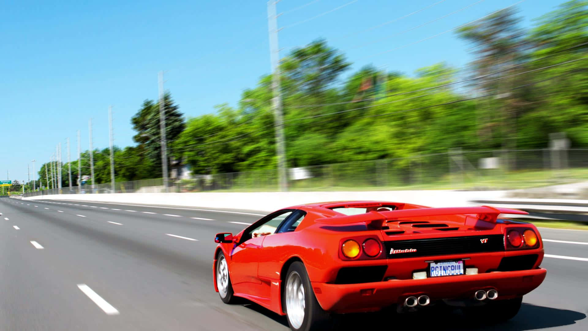 Lamborghini Diablo 桌布 壁紙 — 一輛鮮紅色的藍寶堅尼 Diablo 在陽光明媚的高速公路上疾駛，茂密的綠樹在運動中模糊掠過。