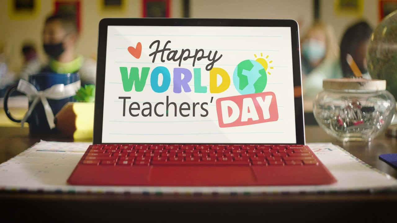  壁紙 — 一台紅色筆記型電腦在書桌上顯示色彩繽紛的「Happy World Teachers' Day」圖案，背景是模糊的教室。