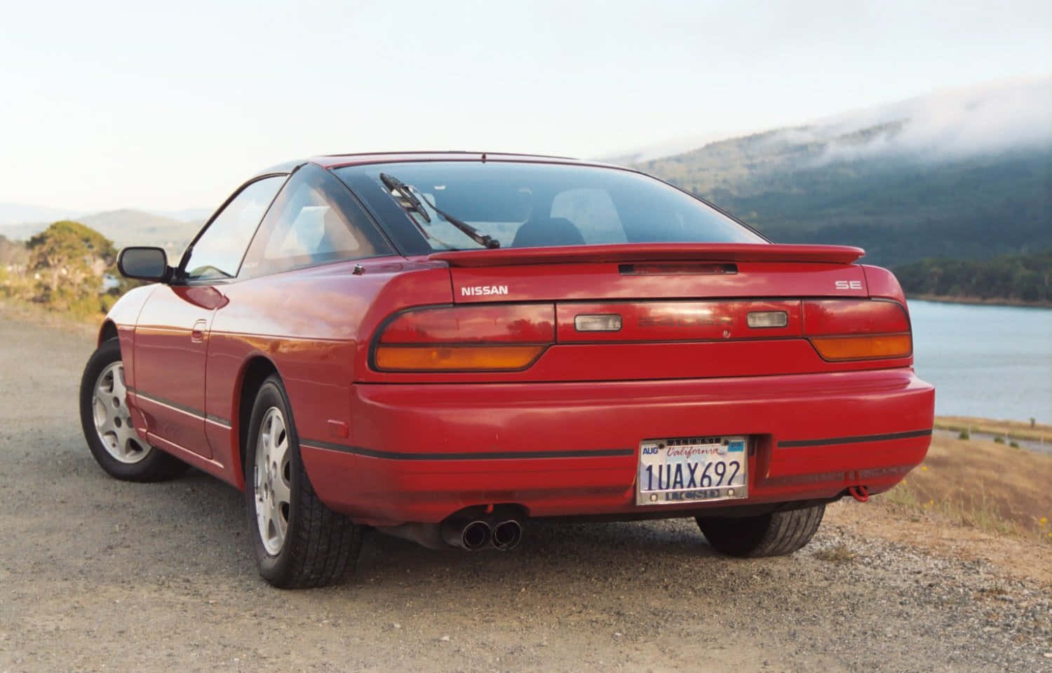  壁紙 — 一輛鮮紅色的日產300ZX SE雙門跑車停在碎石路上，旁邊是霧氣瀰漫的湖泊，背景有山巒。