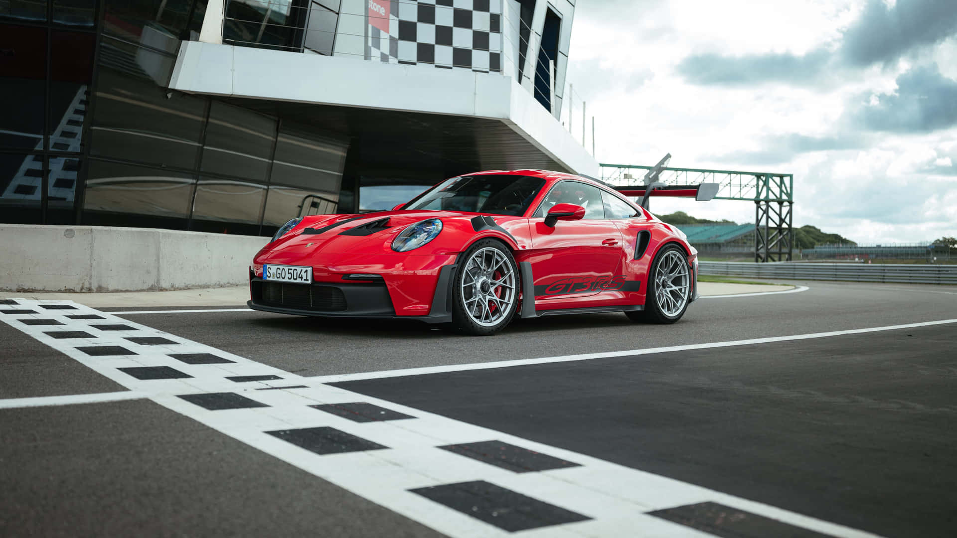  壁紙 — 一輛鮮紅色的保時捷911 GT2 RS停在賽車場上，在陰天穿越方格旗終點線。