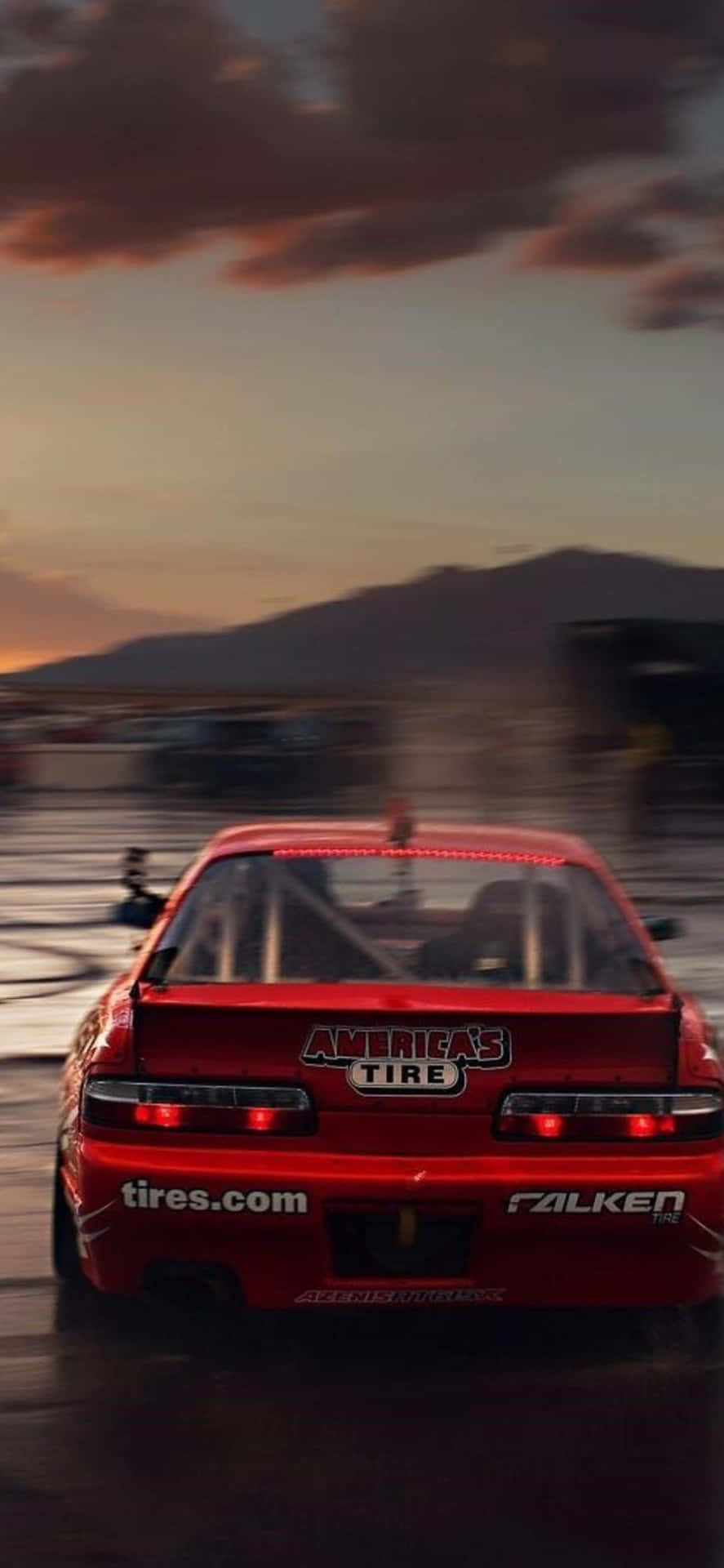 紅色賽車在日落時分的潮濕賽道上漂移，帶有動態模糊效果。 — Project Cars 2 壁紙