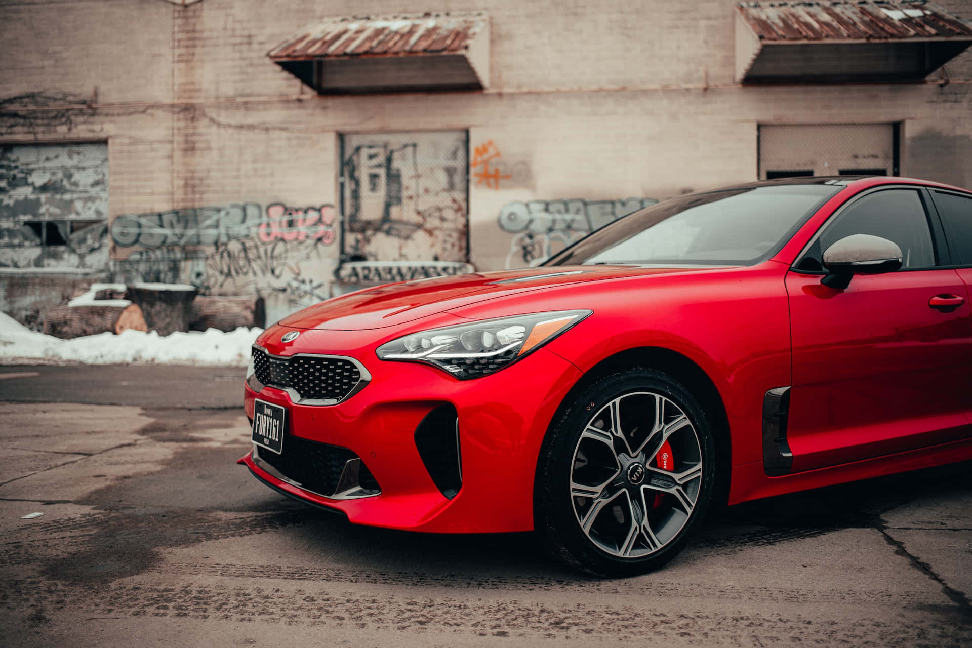 Kia Stinger 桌布 壁紙 — 一輛鮮紅色跑車停放在佈滿塗鴉的市區牆前，地上有積雪。