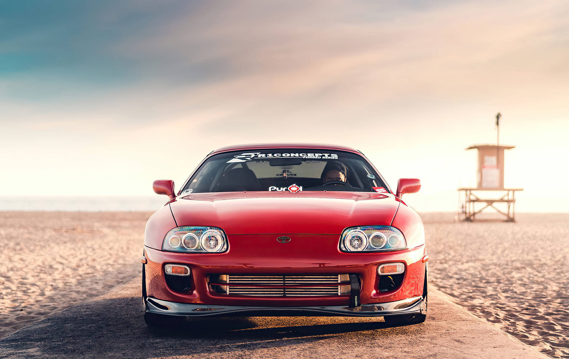 紅色跑車在日落時分停泊在海灘上，靠近救生員瞭望塔。 — Toyota Supra 壁紙