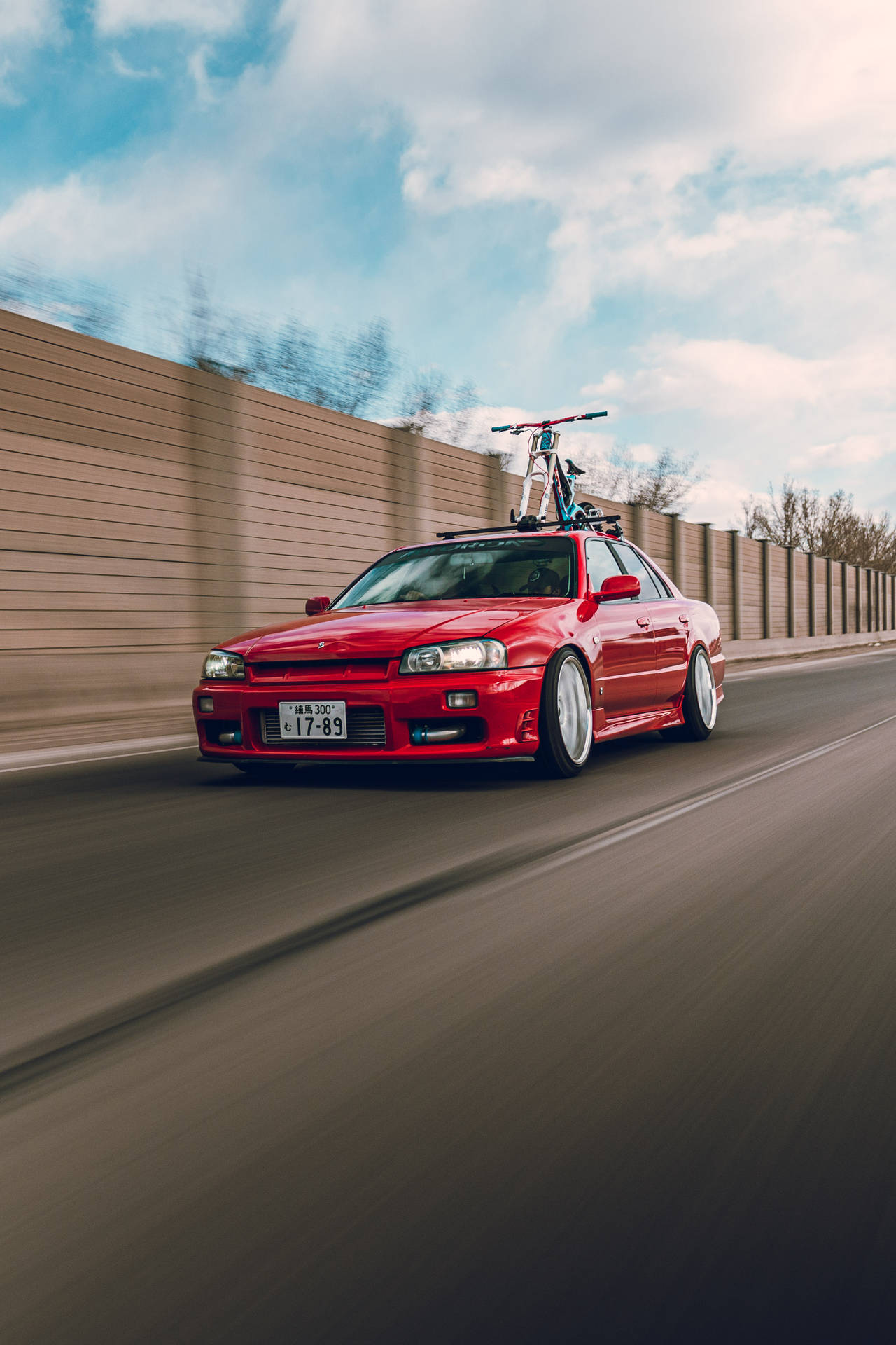 紅色跑車車頂架上載著自行車，在高速公路上疾馳，夕陽時分。 — 日產 Skyline GTR R34 壁紙