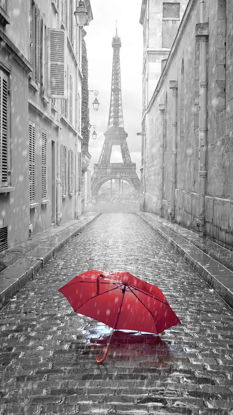  壁紙 — 一把鮮紅色的雨傘在巴黎濕漉漉的鵝卵石街道上打開，遠處霧氣中可見艾菲爾鐵塔。