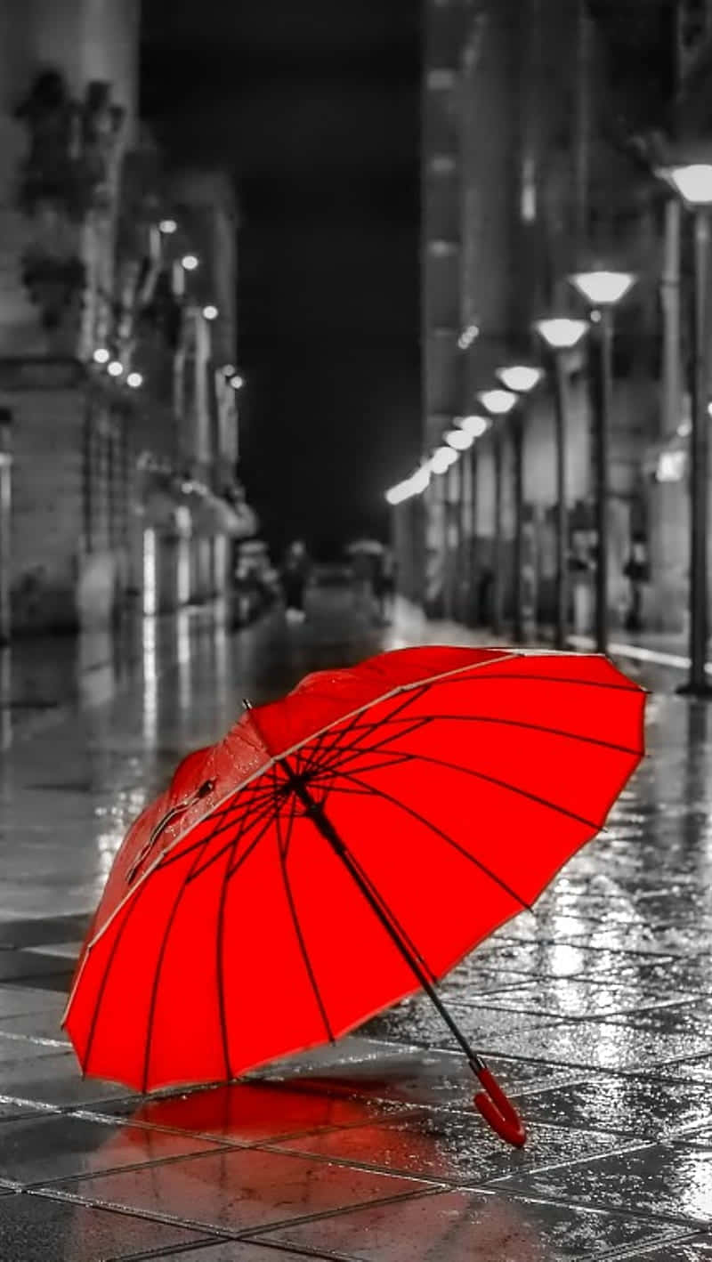  壁紙 — 一把鮮紅色的雨傘在夜晚的濕漉漉城市人行道上，其倒影在街燈下閃爍，呈現黑白場景。