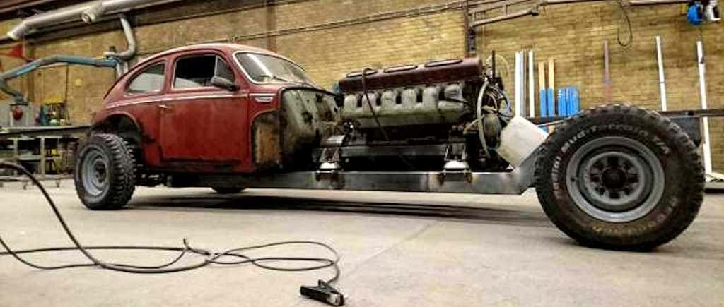 Volvo Pv544 桌布 壁紙 — 一輛紅色復古福斯金龜車，配備巨大的V8引擎和超大輪胎，放置在雜亂車庫的金屬框架上。