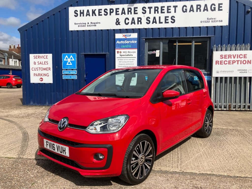  壁紙 — 一輛鮮紅色的Volkswagen up!停放在藍色汽車車庫前，天空清澈湛藍。