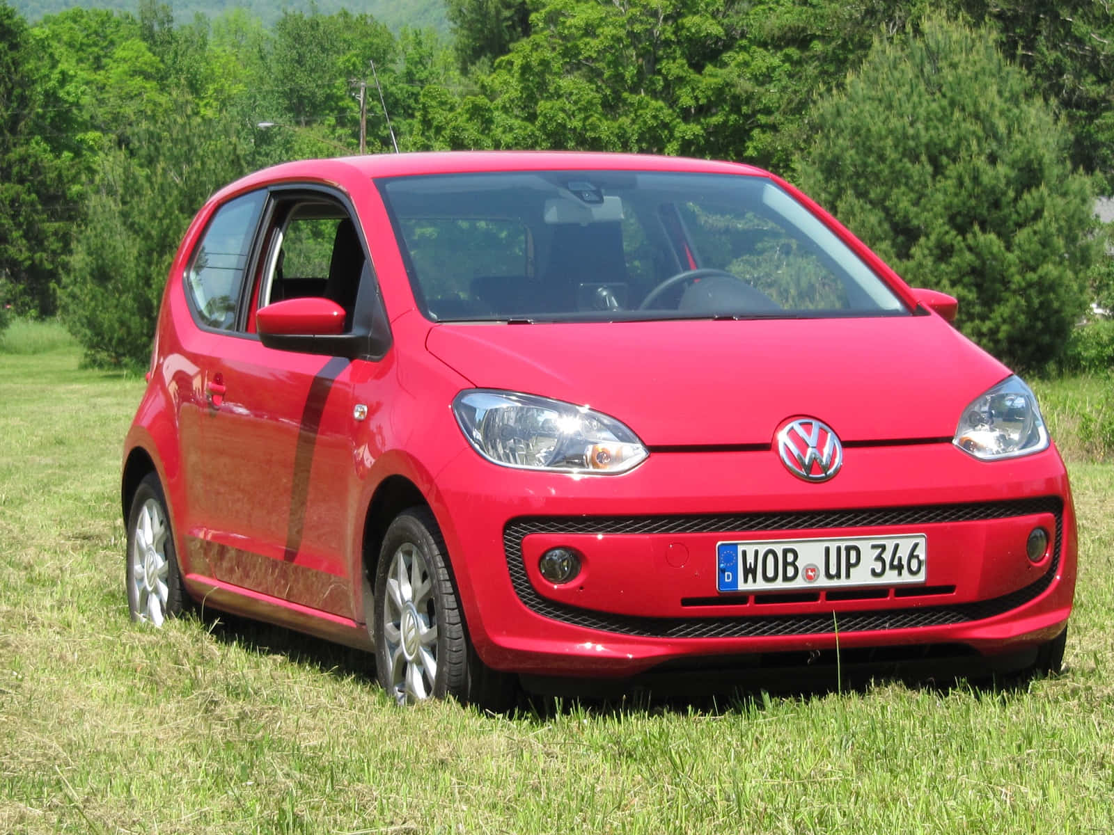  壁紙 — 一輛鮮紅色的Volkswagen up停放在陽光明媚的草地上，背景是茂密的綠樹。