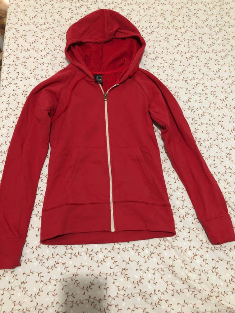 Red Hoodie 桌布 壁紙 — 一件鮮紅色拉鍊連帽上衣，配有白色拉鍊，平放在有圖案的床罩上。